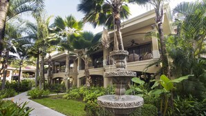 A courtyard with a central fountain, surrounded by palm trees and lush greenery, in front of a multi-story building with balconies. - Great second floor condo with pool view- Best location in Jaco beach (Jaco)