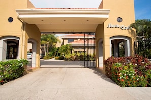 Entrada de un hotel con un paseo techado, palmeras y un camino de entrada portón.
