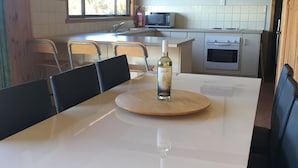 Una cocina con una mesa de comedor, sillas, un microondas, un horno y una botella de vino sobre la mesa.