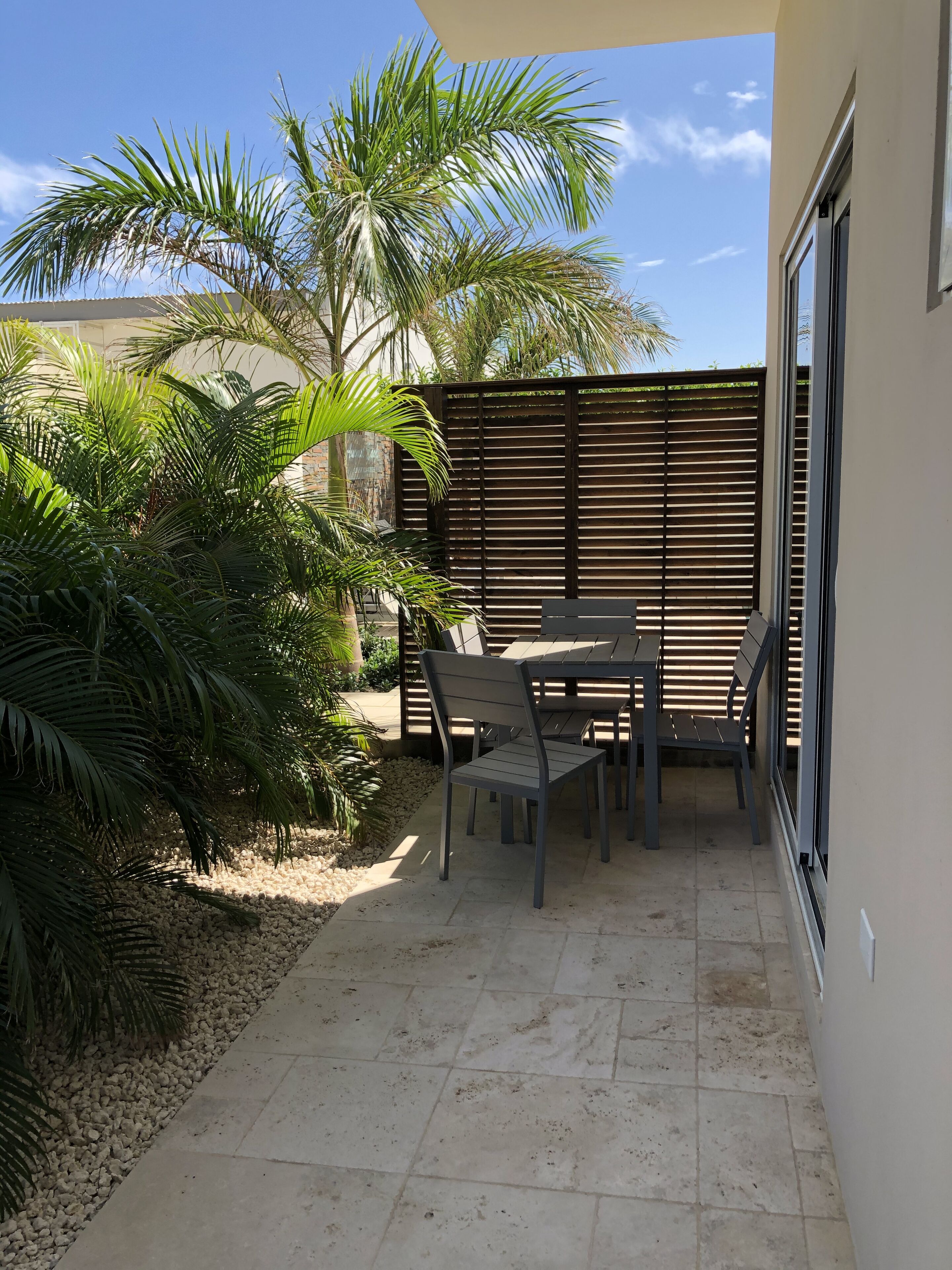 Ein Patio mit Tisch und Stühlen, umgeben von Palmen und einem Holzzaun.