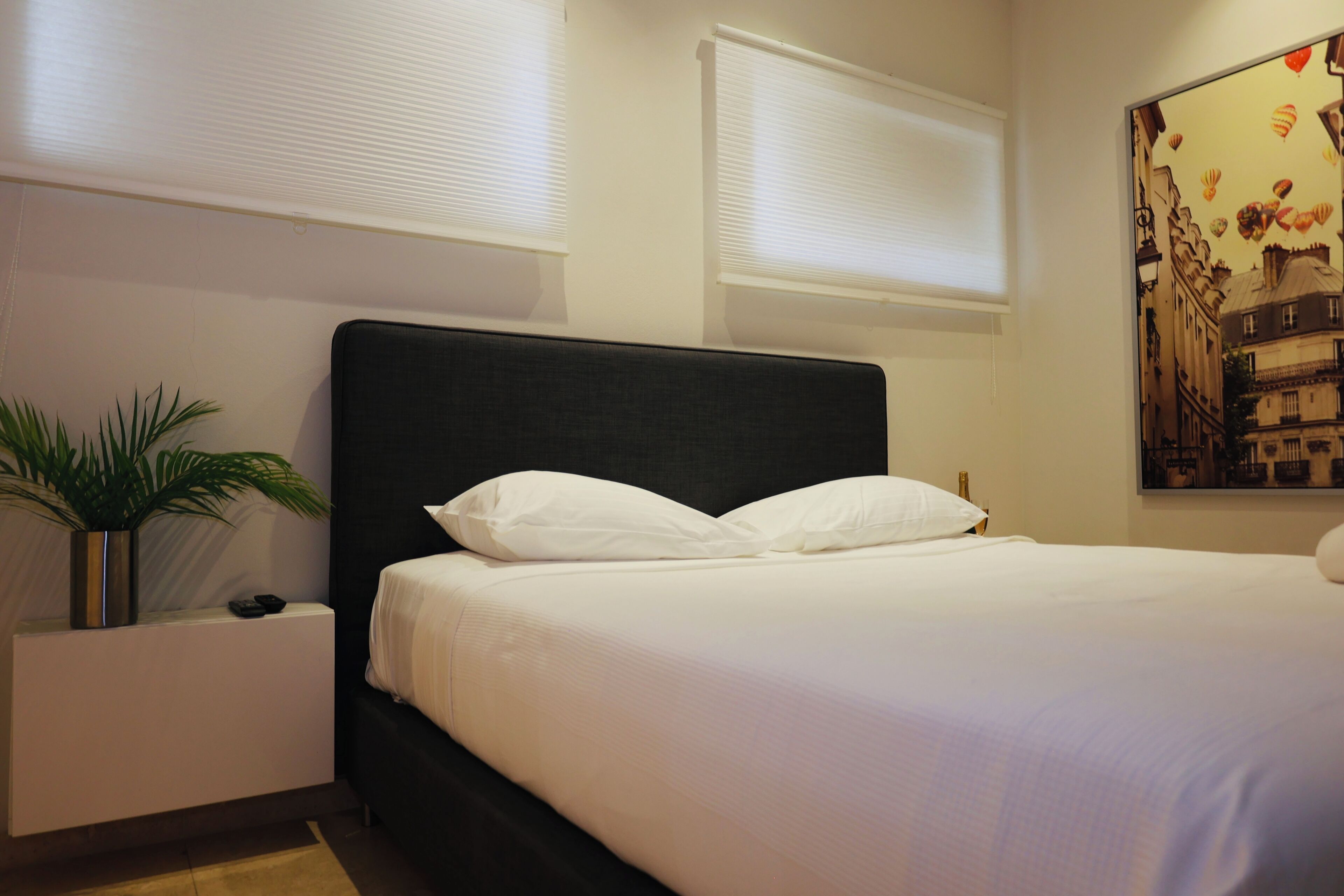 Una habitación de hotel con una cama grande, una mesita de noche con una planta y una obra de arte colgada en la pared.