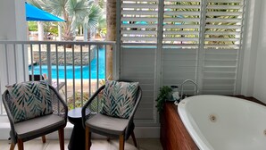 A balcony with two wicker chairs, a small table, and a view of a swimming pool and palm trees. - Ground floor, Poolside Luxury Apartment (Palm Cove)