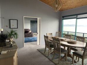A dining area with a wooden table and chairs, a view of the outdoors, a sofa in the background, and a framed certificate on the wall. - Harbour views from super spacious upstairs apartment. Fully equipped. (Onerahi)