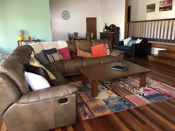 A living room with a sectional sofa, a coffee table, a patterned rug, and a dining area with chairs and a table.