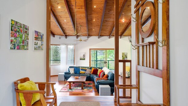 Un vaste espace de vie doté d’un plafond en bois, d’un grand canapé, d’une table basse et offrant une vue sur l’extérieur grâce à de grandes fenêtres.