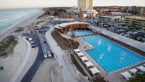 Ein Küstenhotel mit großem Pool, einer Promenade direkt am Strand und einem Parkplatz.