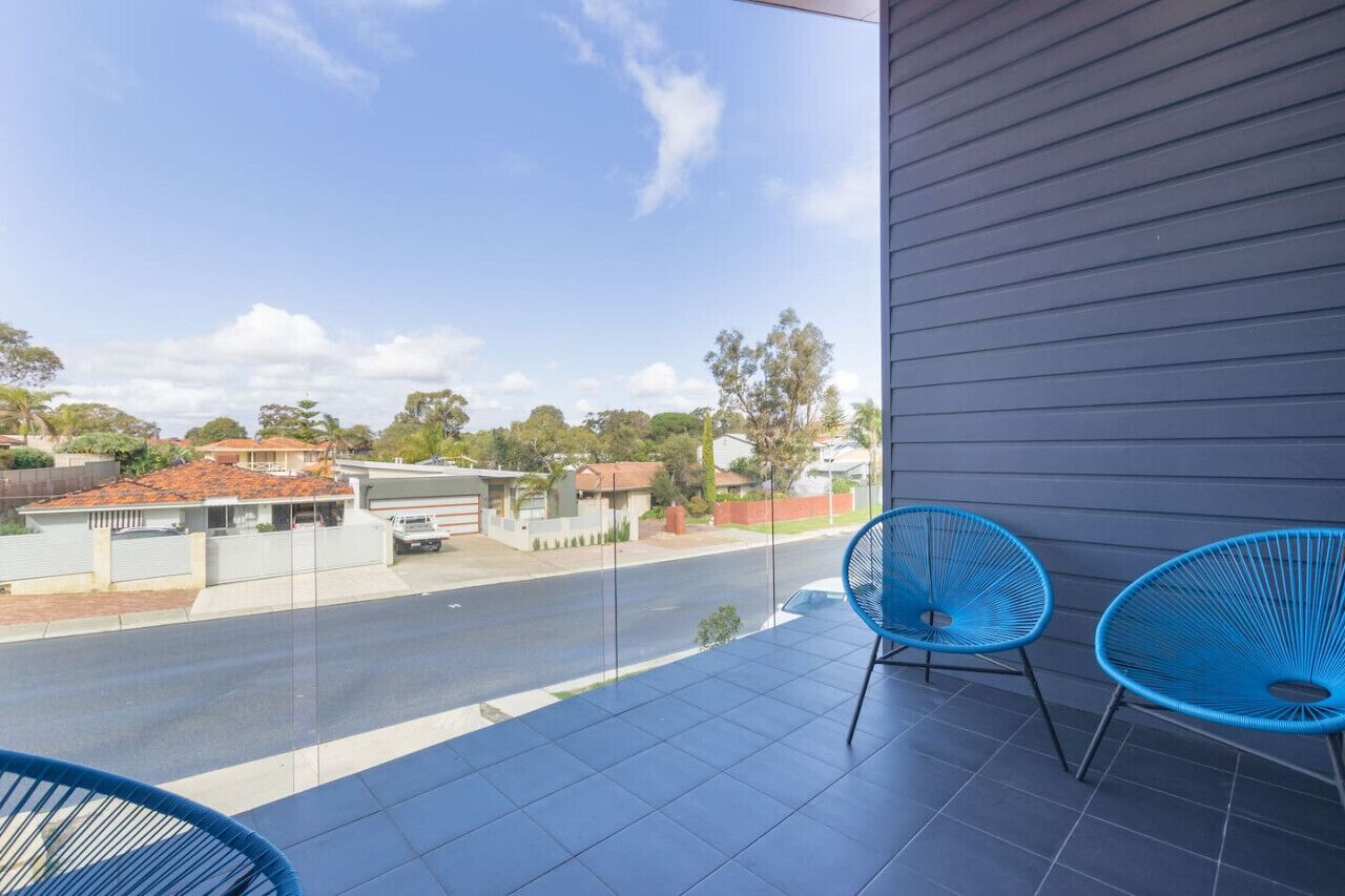 A balcony with two blue chairs, a view of a street, and houses in the background.