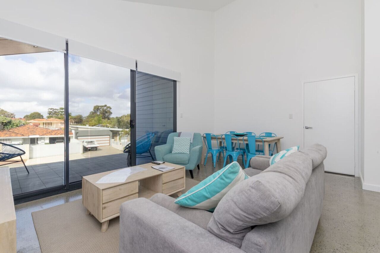 A modern living room with a grey sofa, a wooden coffee table, and a dining area with blue chairs and a table.