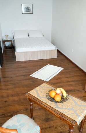 A bedroom with a bed, a bedside table with a lamp, a chair, and a table with fruit.