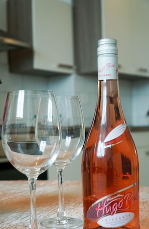 A bottle of Hugo Rosé wine and two empty wine glasses on a wooden surface.