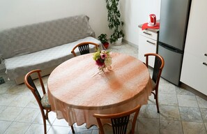 A compact living space with a round table, two chairs, a sofa, a refrigerator, and a potted plant.