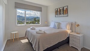 Een slaapkamer met een bed, nachtkastje, raam met uitzicht en een kunstwerk aan de muur.