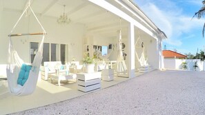 Relax in a tranquil outdoor space with a covered patio featuring cushioned hanging chairs and comfortable sofas.