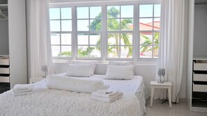 Relax in a serene space with a large bed, white linens, and a view of lush greenery.