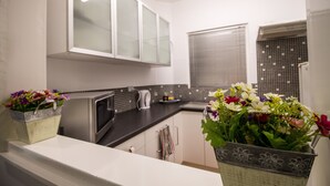 A modern kitchen with white cabinets, a microwave, and a kettle. There are two flower baskets on the counter. - M107 CBD Location near Kings Park  (West Perth)