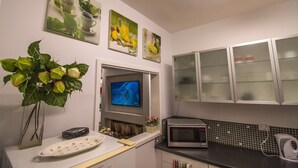 A kitchen with a microwave, a kettle, and a TV mounted on the wall. There are cabinets with glass doors and a plant on the counter. - M107 CBD Location near Kings Park  (West Perth)