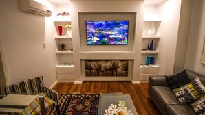 A living room with a flat-screen TV, a fireplace, a sofa, a coffee table, and a patterned rug. - M107 CBD Location near Kings Park  (West Perth)