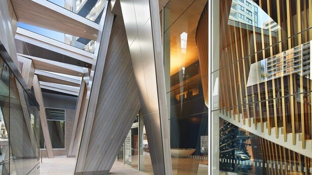 Un bâtiment moderne doté d’une façade en verre, d’un escalier avec des rampes en bois et d’un design géométrique.
