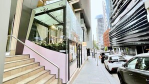 Un bâtiment moderne doté d’une façade en verre, d’un escalier et d’un espace de stationnement où sont garées des voitures.