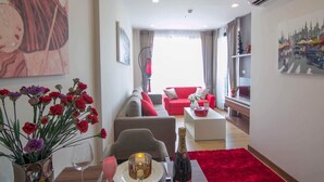 A modern living room with a red sofa, a dining table with a vase of flowers, and a cityscape painting on the wall. - Romantic Honeymoon Siam Suite, Central Chiang Mai (Tambon Chang Khlan)