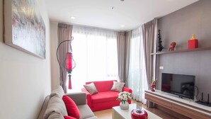 A modern living room with a red sofa, a grey sofa, a coffee table with decorative items, a flat-screen TV, and a large window with sheer curtains. - Romantic Honeymoon Siam Suite, Central Chiang Mai (Tambon Chang Khlan)