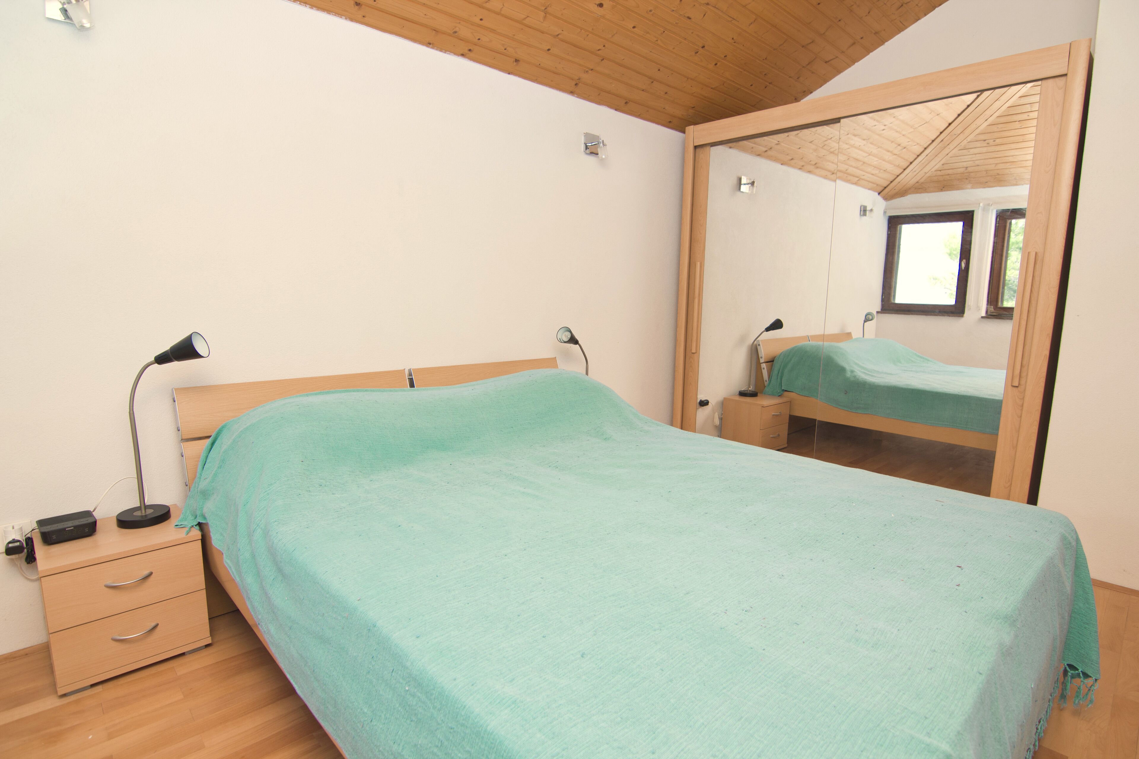 Une chambre à coucher avec un lit, une table de chevet, un miroir et une fenêtre.