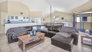 A spacious living area with a large L-shaped sofa, a wooden coffee table, and a kitchen in the background. - Sail Away - Aldinga Beach - C21 SouthCoast Holidays (Aldinga Beach)