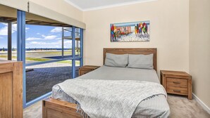 A bedroom with a large window, a bed, a nightstand, and a painting on the wall. - Sail Away - Aldinga Beach - C21 SouthCoast Holidays (Aldinga Beach)