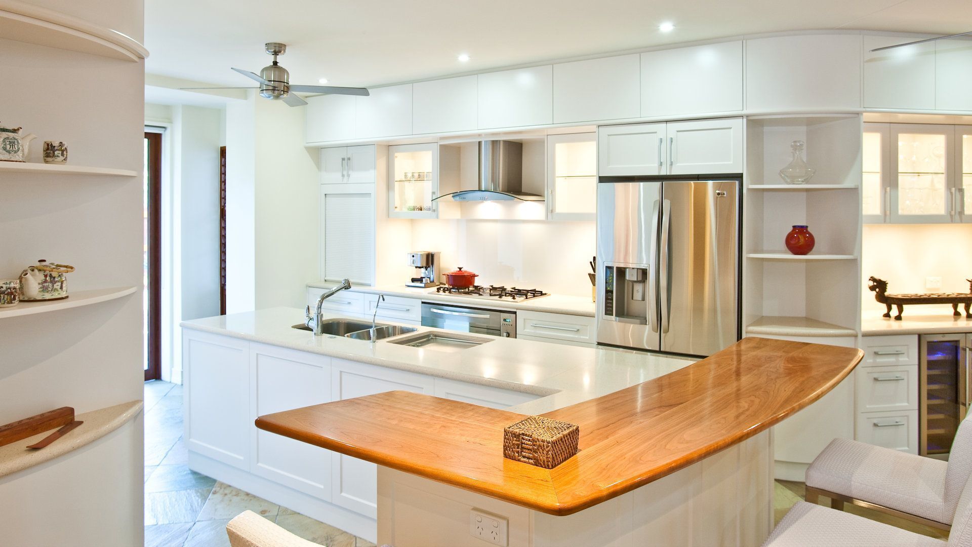 A modern kitchen with white cabinetry, a stainless steel refrigerator, and a wooden countertop.