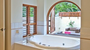 A bathroom with a large bathtub, wooden window shutters, and a view of an outdoor seating area. - 7 Solander Boulevard, Port Douglas QLD 4877 (Port Douglas)