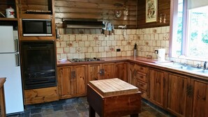 A kitchen with wooden cabinets, a microwave, an oven, a wooden cutting board, and a window with a view of greenery. - View Mount - Families and small groups (Merrijig)