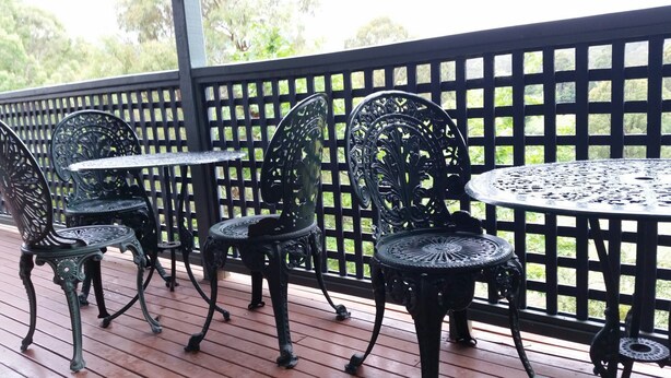 A patio with ornate metal chairs and tables, a wooden deck, and a lattice fence. - View Mount - Families and small groups (Merrijig)