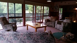 A spacious living room with a large window, a wooden coffee table, floral-patterned sofas, and a view of a deck with outdoor furniture. - View Mount - Families and small groups (Merrijig)