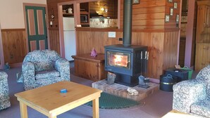 A cozy living room with a wood-burning stove, patterned furniture, and a green door. - View Mount - Families and small groups (Merrijig)