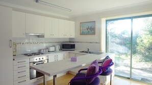A modern kitchen with white cabinets, a central island, a microwave, and a large window. - Moon House - family bungalow (Diamond Creek)