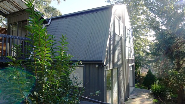 A modern building with a sloped metal roof, surrounded by lush greenery and trees. - Moon House - family bungalow (Diamond Creek)