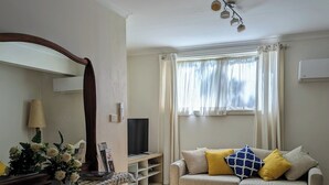 A living room with a sofa, a coffee table, a TV, and a window with curtains. - Moon House - family bungalow (Diamond Creek)