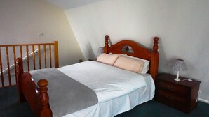 A bedroom with a wooden bed, a nightstand, a lamp, and a staircase. - Moon House - family bungalow (Diamond Creek)