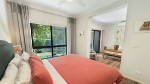 Un dormitorio con una cama grande, vistas al exterior, un ventilador de techo y una pequeña mesa con una silla.