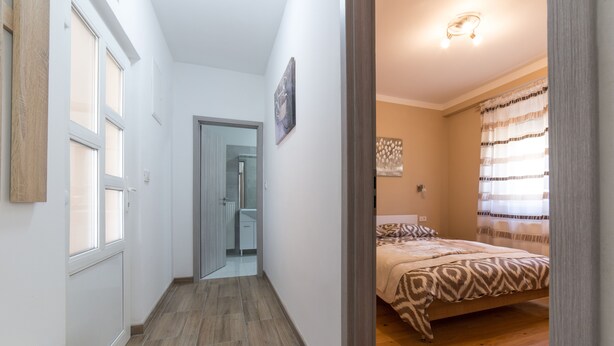 A bedroom with a bed, a wooden floor, and a door leading to a bathroom. - Apartment Raspolic - no.1 (Trinajstici)