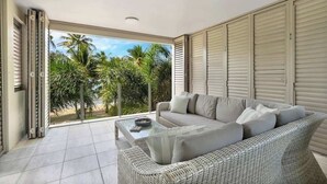 A modern living room with a sofa, a glass coffee table, and a view of palm trees. - Rojo at Island Views—A Breezy Beachfront Retreat (Palm Cove)