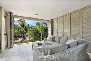 A modern living room with a sofa, a glass coffee table, and a view of palm trees.