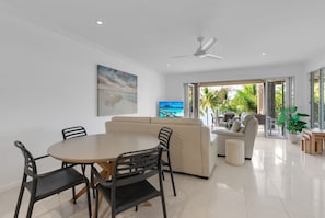 A modern living room with a round dining table, beige sofa, and a ceiling fan.