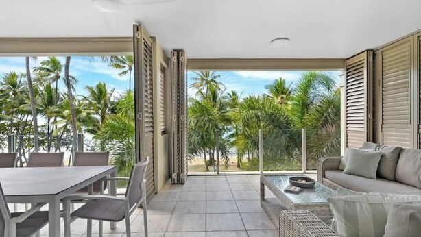 A balcony with a dining table and chairs, a sofa, and a view of palm trees. - Rojo at Island Views—A Breezy Beachfront Retreat (Palm Cove)