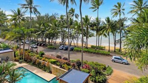A pool, palm trees, a beach, and a road with parked cars. - Rojo at Island Views—A Breezy Beachfront Retreat (Palm Cove)