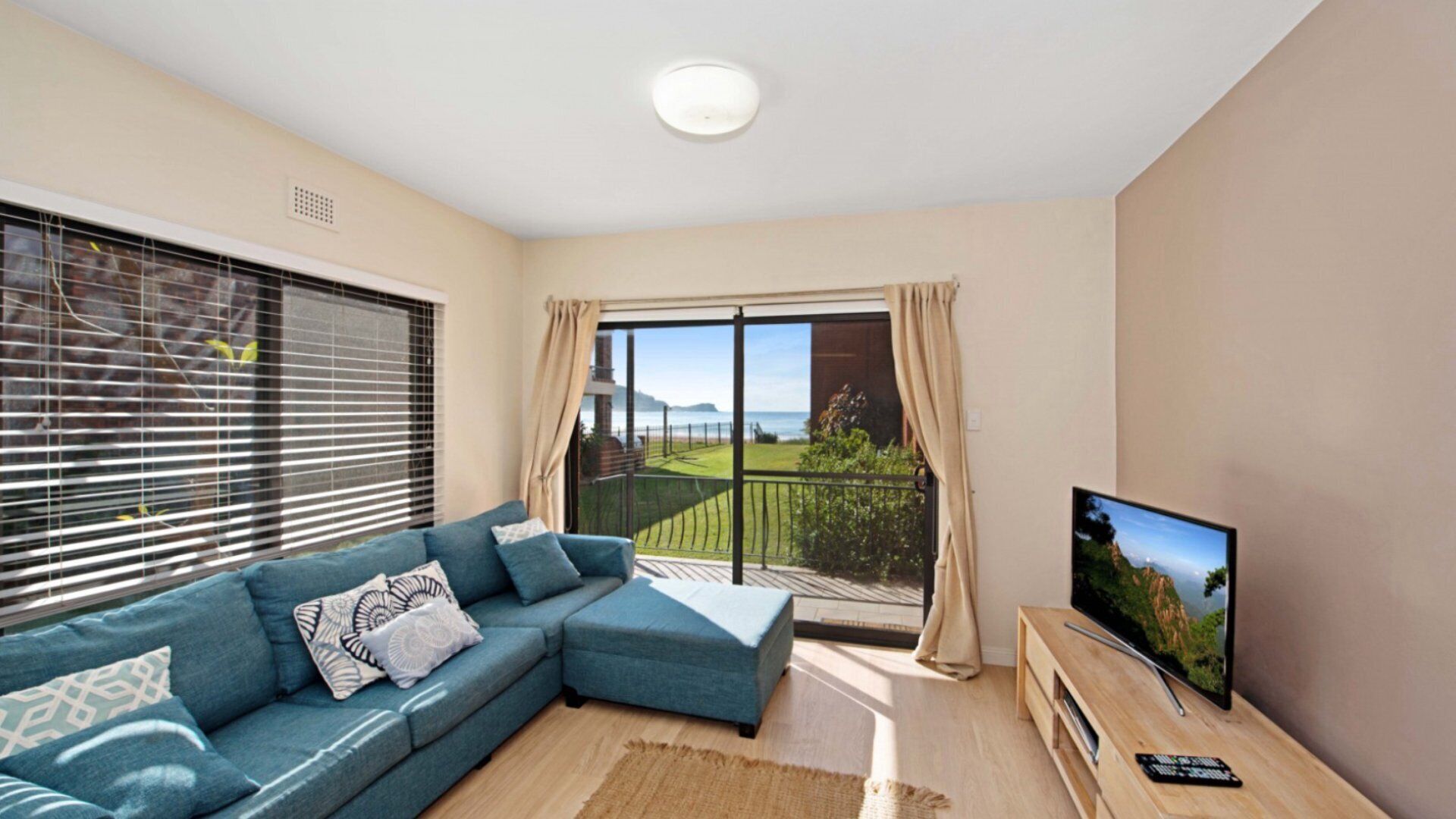 A living room with a blue sofa, a TV, and a balcony with a view of the sea.
