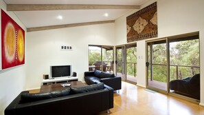 A modern living room with a flat-screen TV, black leather sofas, and large sliding glass doors leading to a deck.