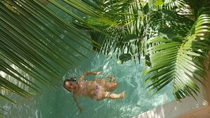 En person flyder i en klar pool omgivet af palmer.