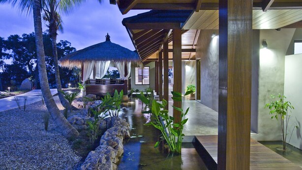 A modern resort with a thatched-roof structure, a water feature, and a covered seating area.