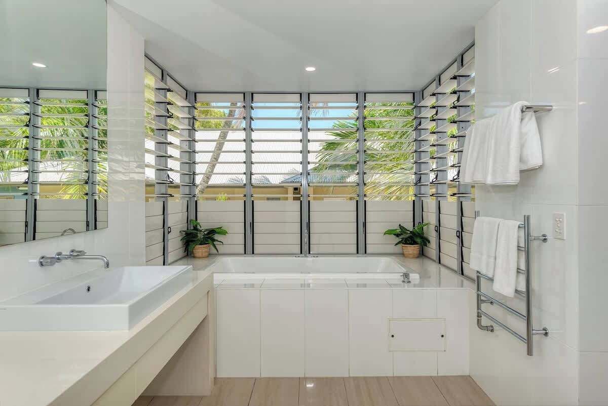 Een moderne badkamer met een groot ligbad, een witte wastafel en een spiegel. Op het aanrecht staan twee potplanten.